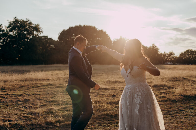 Bride and groom dance together in a field at sunset