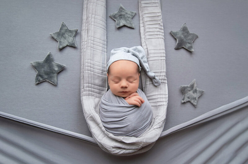newborn baby boy wrapped in grey with a grey sleepy hat with stars around for his Burlington newborn photos.