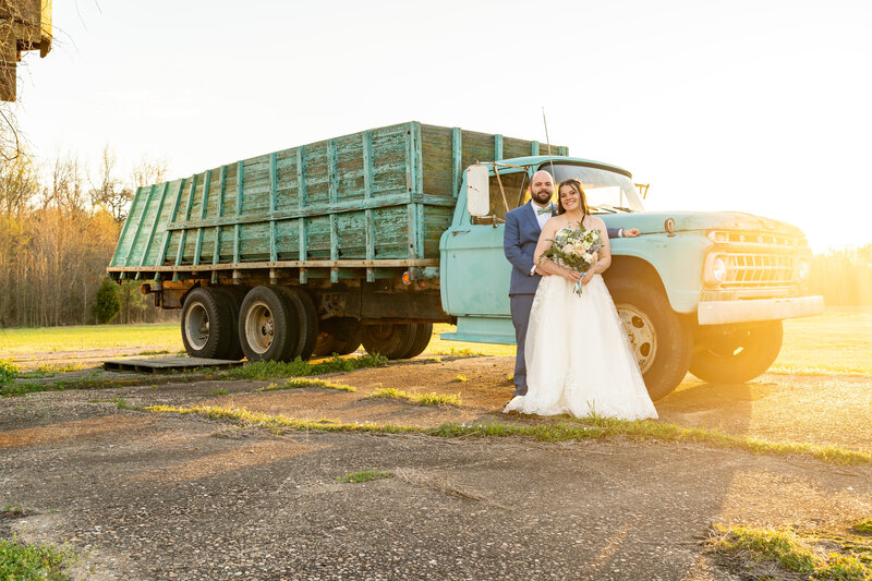 Bride and groom standing in front of vintage farm truck during their wedding day couples portraits.