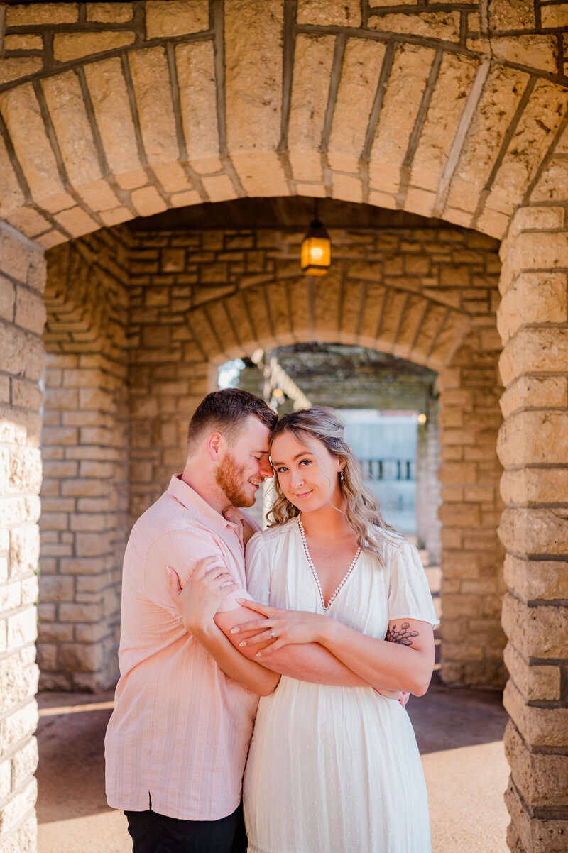 Man wraps arms around woman and woman looks directly at the camera.