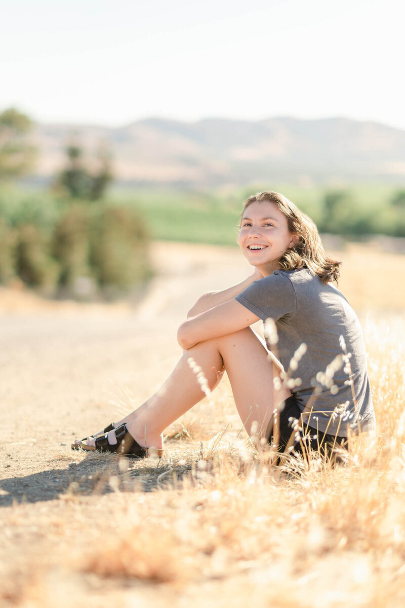 High school senior girl sitting by the side of the road at Holdener Park in Livermore, CA; photo by Livermore senior photographer Kristen Hazelton