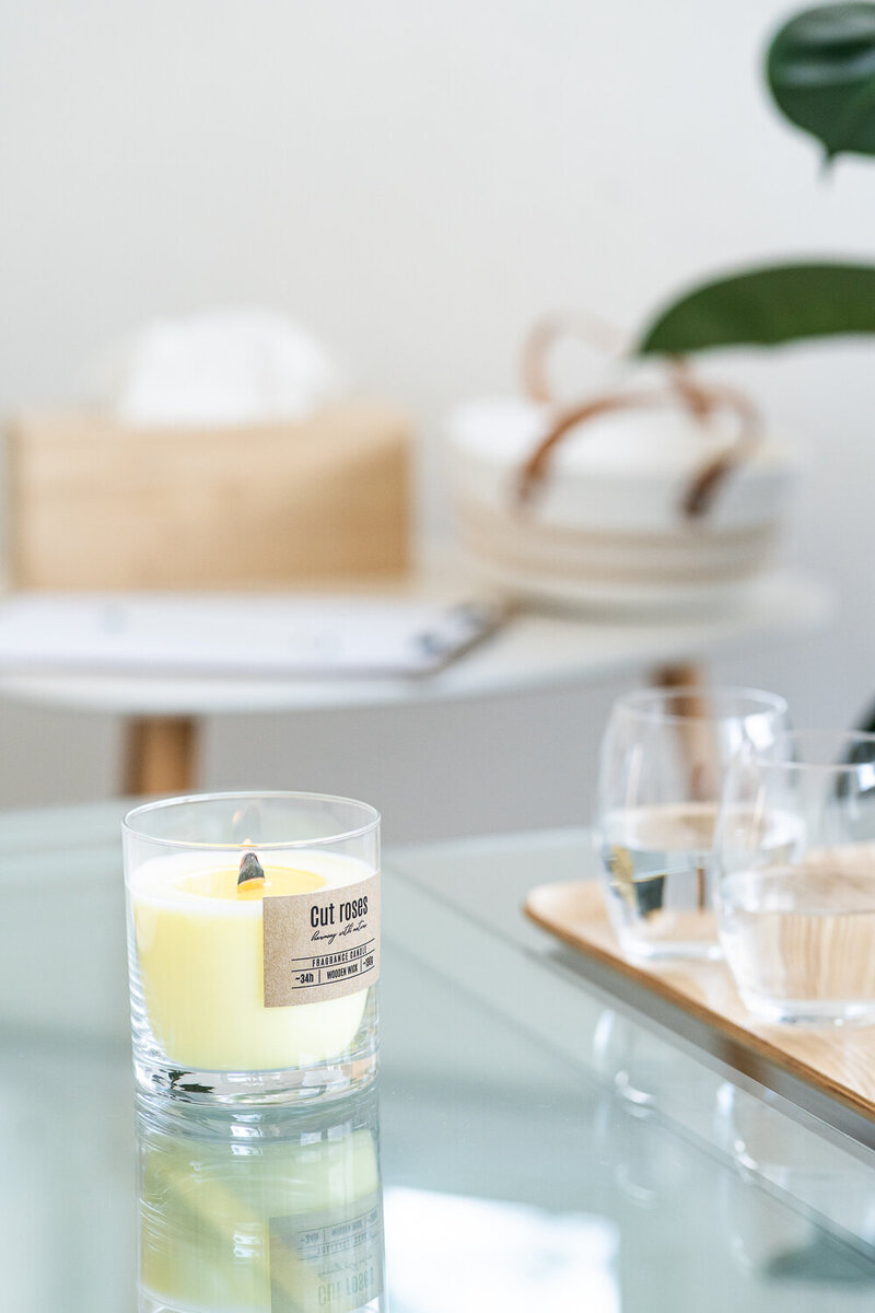 zapálená svíčka stojí na skleněném stole, vedle ní jsou sklenice s vodou