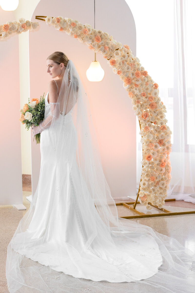 bride standing in bridal gown in front of arched flowers