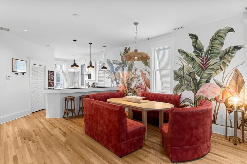 Inviting dining area with vibrant red booths and tropical flamingo mural at The Florida House, located near Panama City Beach and Santa Rosa Beach vacation rentals.