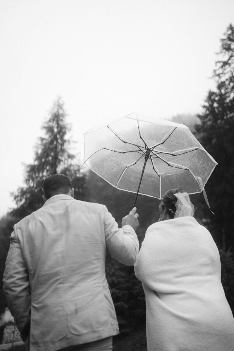 Groom holds umbrella over bride as it rains during their Dolomites elopement