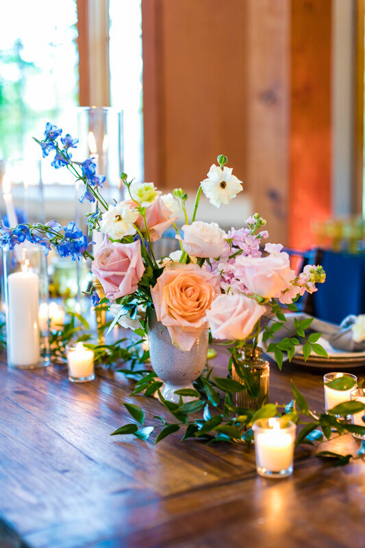 Romantic wedding centerpiece with soft pink roses, blue flowers, and candlelight on a wooden table, styled by an Austin wedding planning expert.
