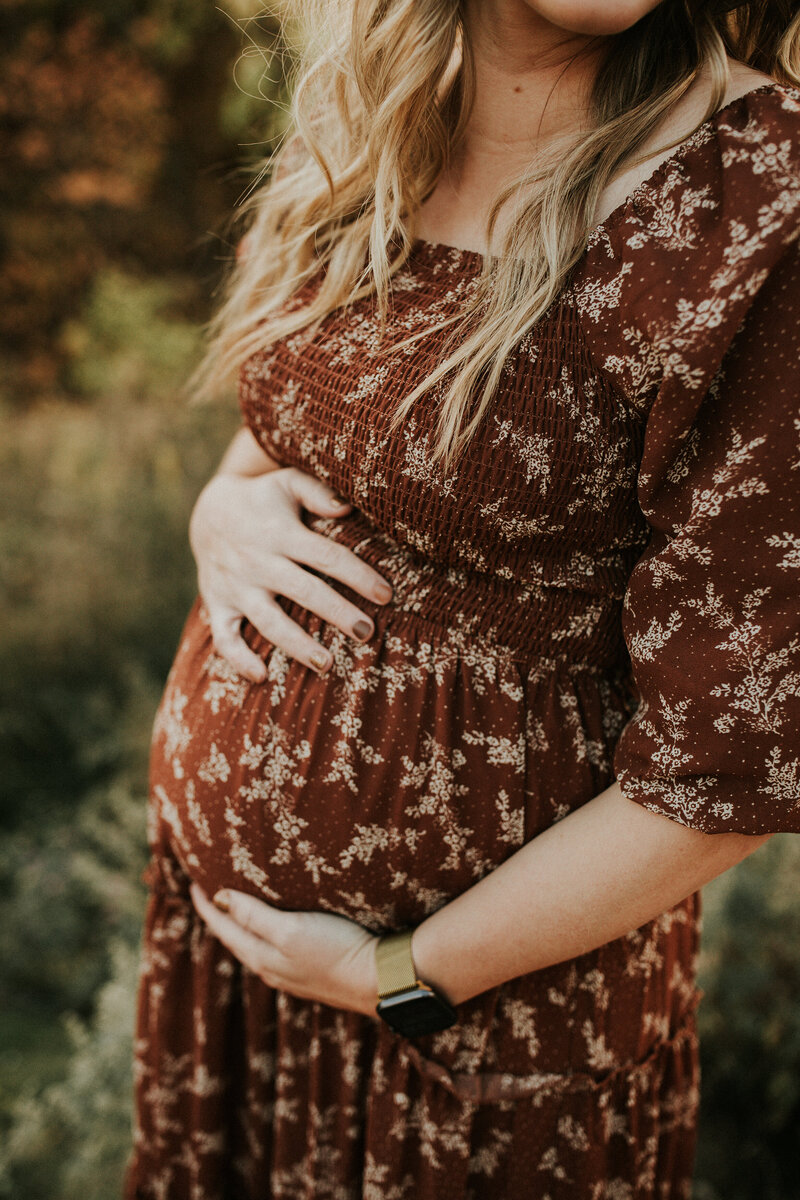 A woman in a red floral dress holds her baby bump