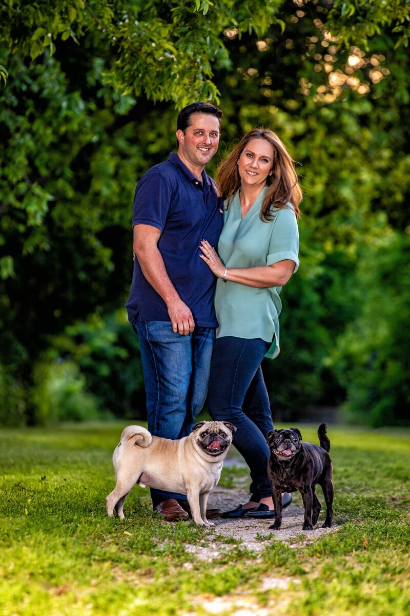 Couple poses under a tree at Cedar Hill State Park with their pugs.