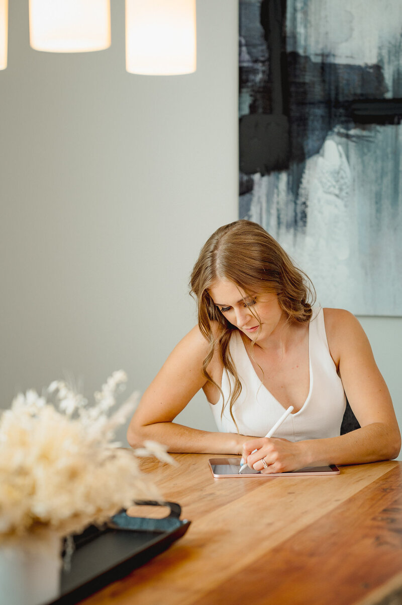 Woman sitting at table writing on an ipad