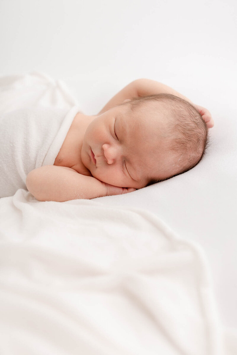 light-skinned baby sleeping peacefully tucked under a white swaddle - Portland Newborn Photography Studio