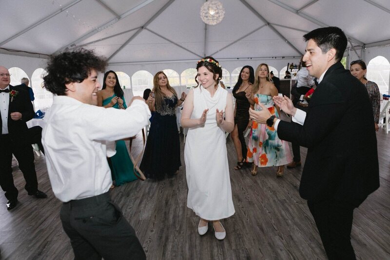 A newly married couple dance with their friend at their reception as others look on.