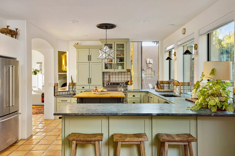 Eclectic kitchen in Cave Creek with patterned ceramic tile backsplash, star pendant light, dark soapstone counters, a butcher block island and sage green cabinets.