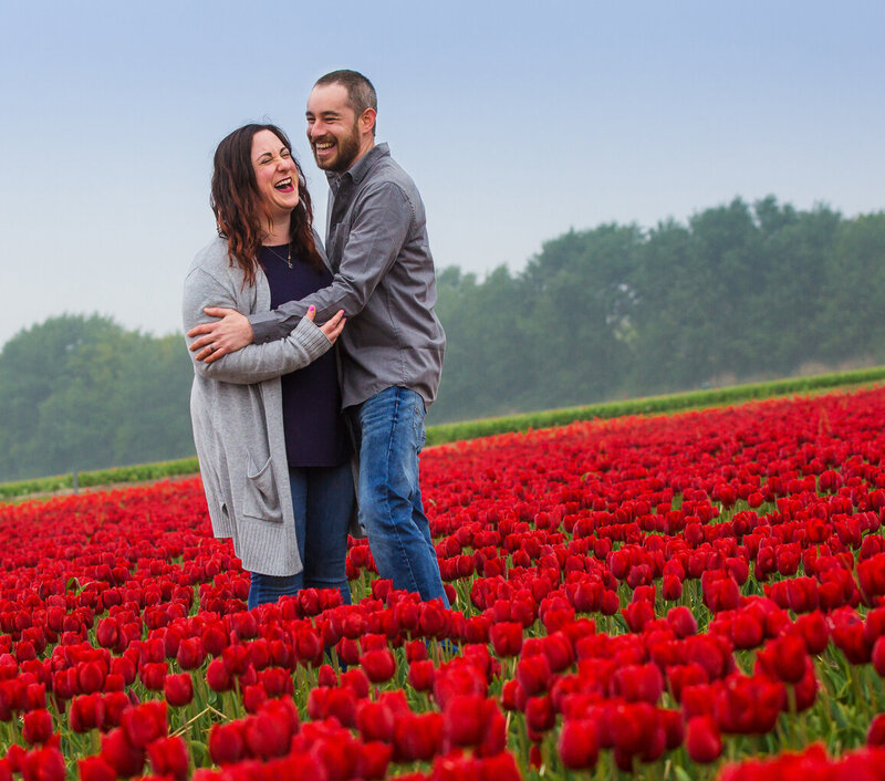 An engaged couple in a field of red tulips.