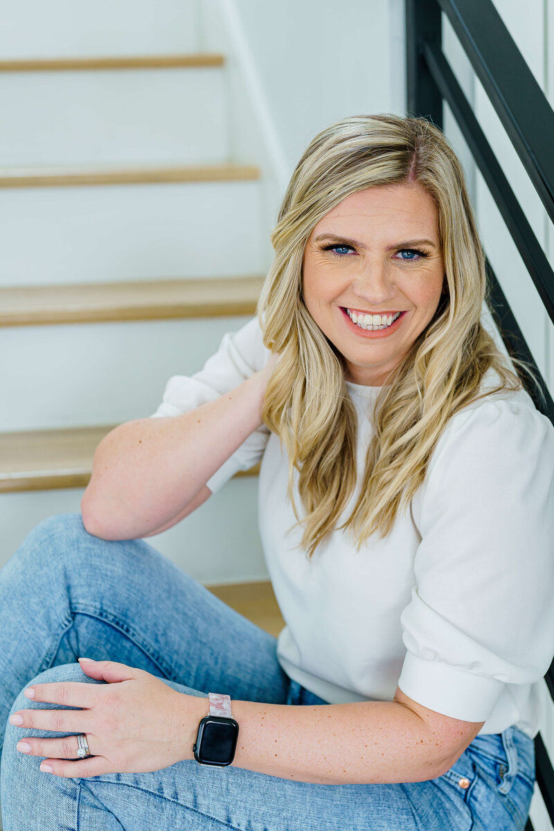 Claire Thom sitting on stairs holding her blond hair away from face