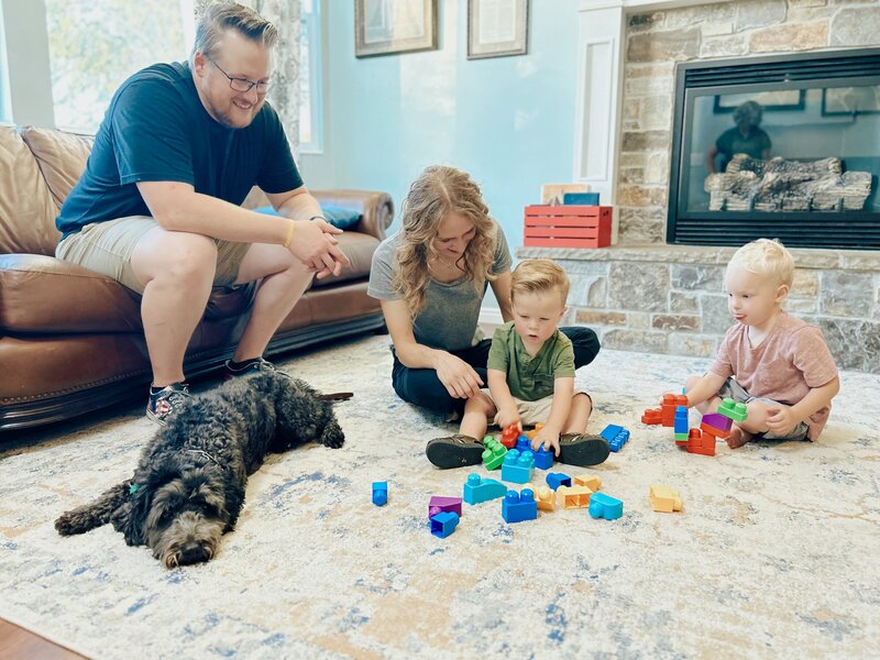 2 kids, a man, and a woman playing with blocks while their dog lays calmly in a down command