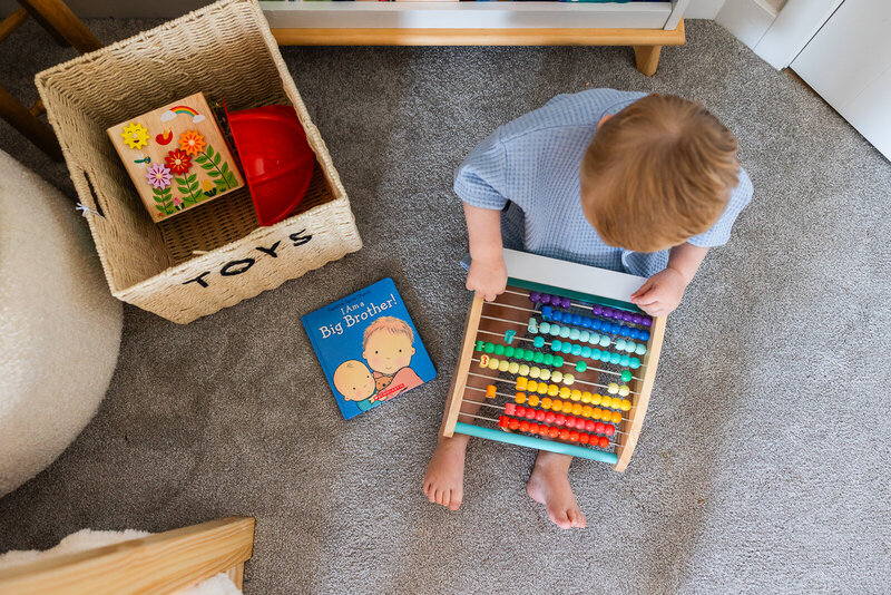 Little boy playing with toys in his bedroom next to his toybox that says TOYS during a family session at home. 