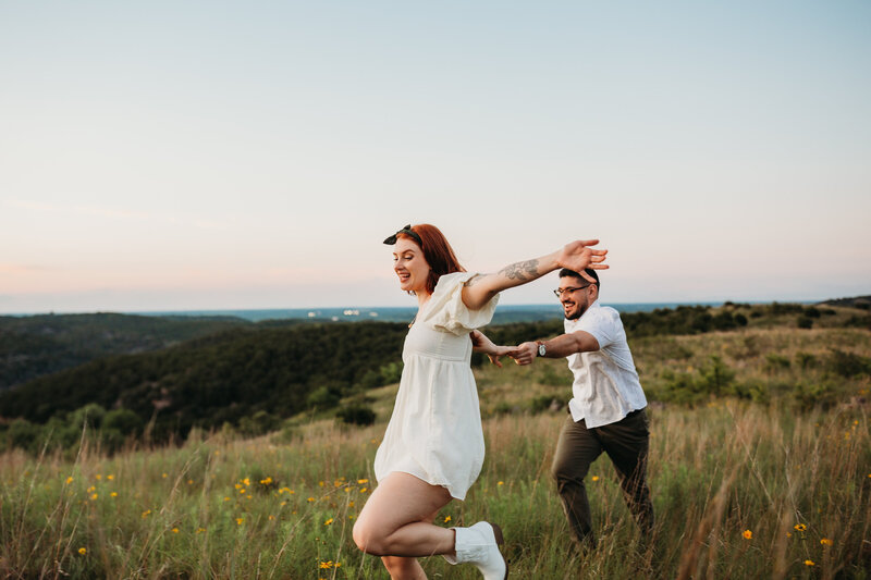 Joyful couple running through a field at sunset, with the woman leading and looking back with a carefree expression