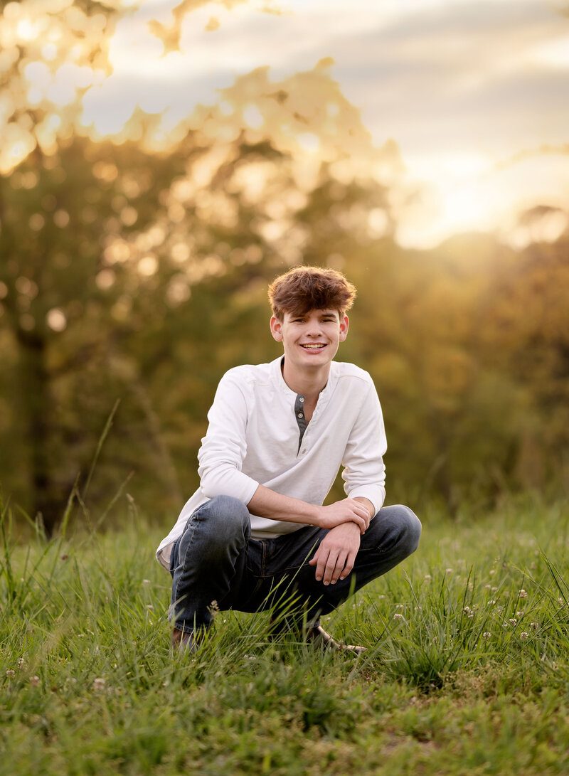 Graduation portrait of boy kneeling in an open field near Atlanta GA. Photo was taking by Senior photographer Jenni Nikki Photography.