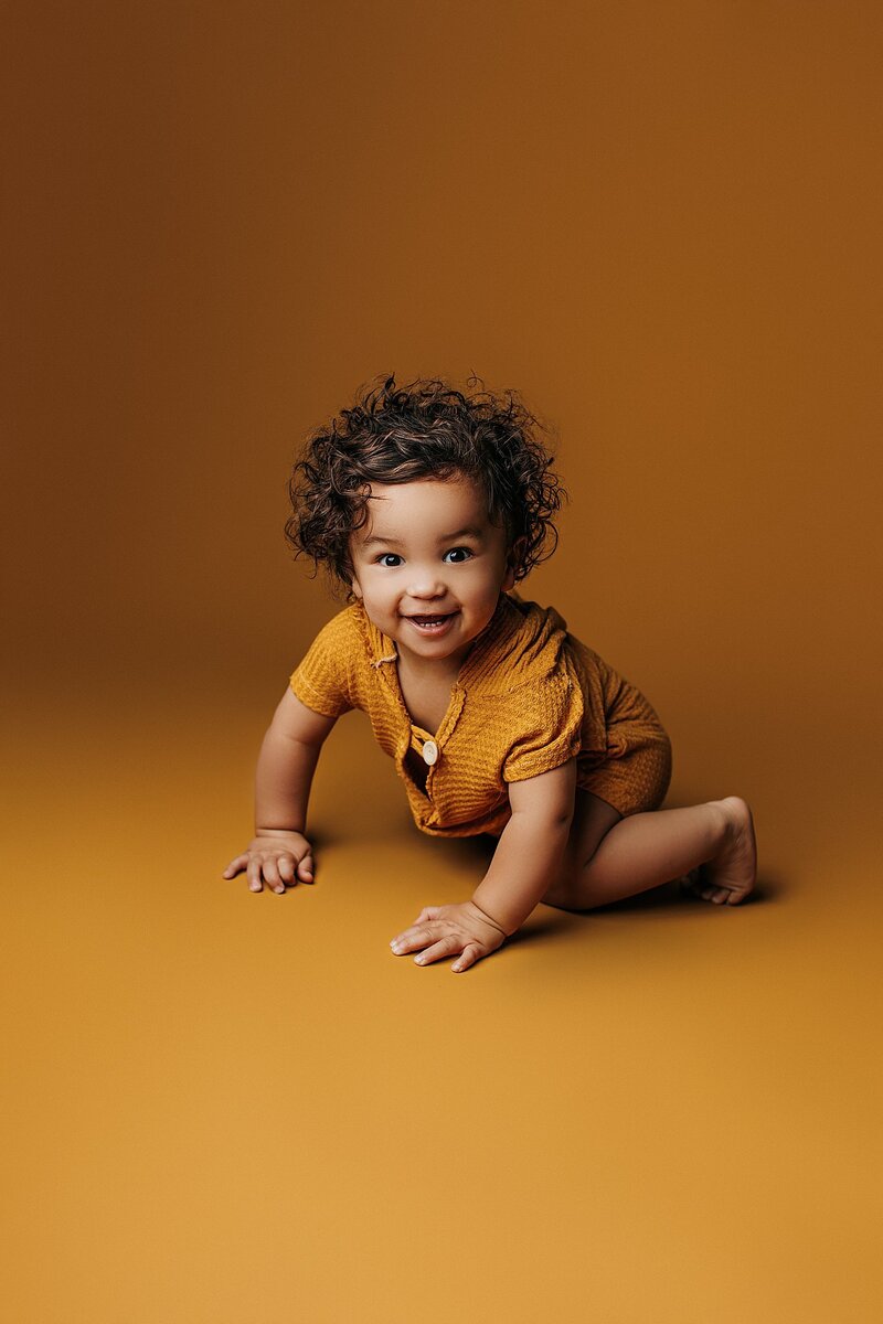 Smiling baby on mustard yellow backdrop during fun milestone session