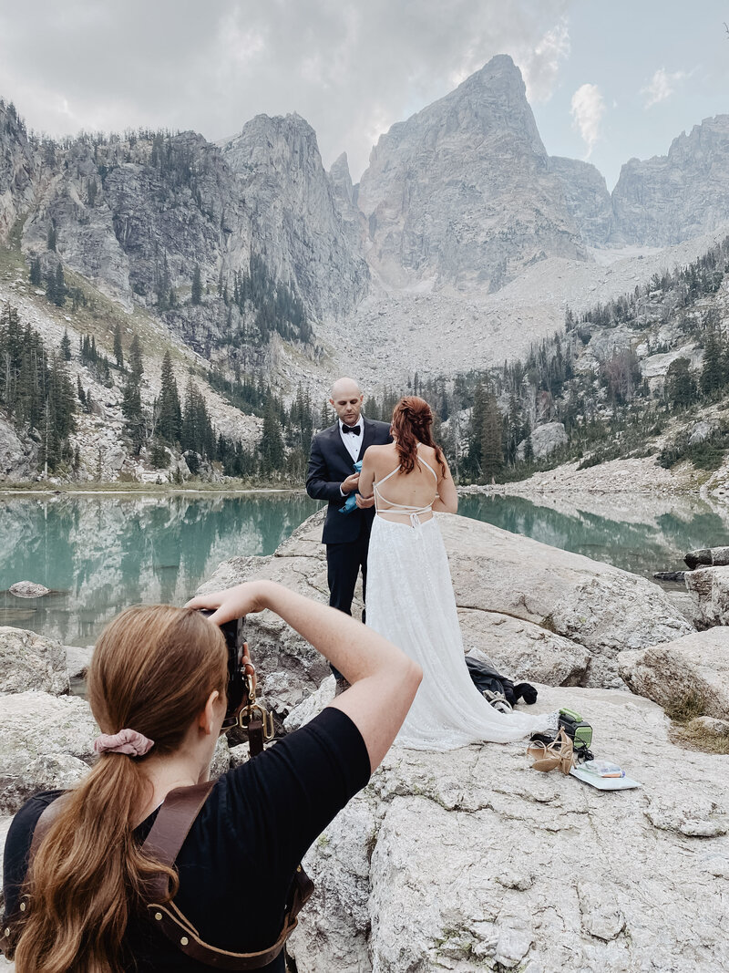jackson hole photographers captures bride and groom in front of the tetons at delta lake for a spring wyoming elopement on a cloudy day