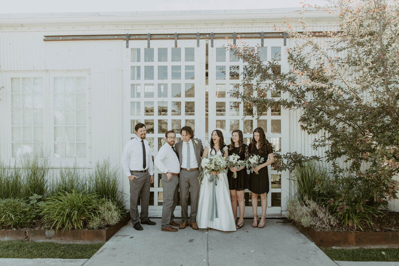Bridal party laughing together in front of white barn doors at the White Shanty Venue in Provo, Utah.