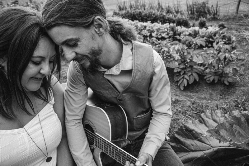 couple leans foreheads together holding a guitar