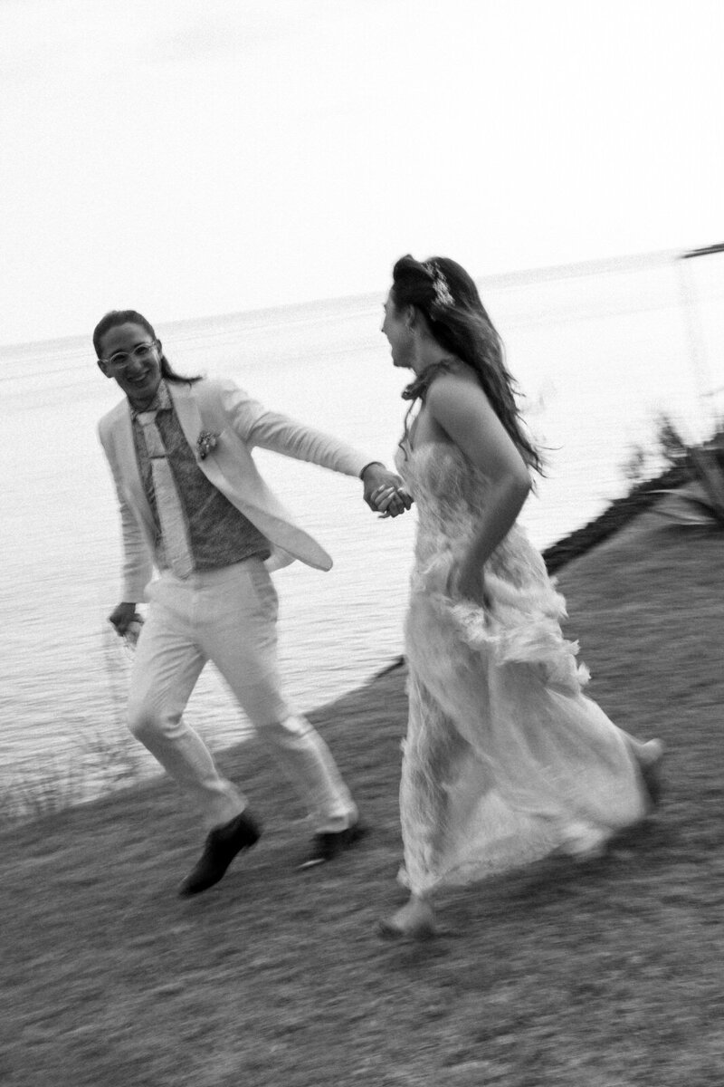 Bride and Groom joyfully running while holding hands on the Azores Islands of Portugal coast, documented by Andrea-Marie Photography