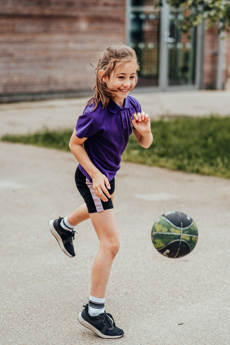 Girl from Cambridge Primary school playing basket ball on school playground