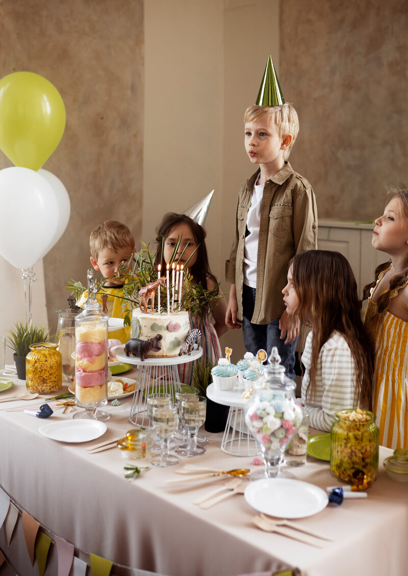 Organisation d'anniversaire. Enfants debouts autour d'une table décorée sur le thème jungle