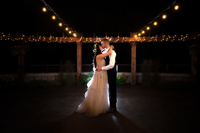 Bride a groom kiss in a night time shot among strings of cafe lights