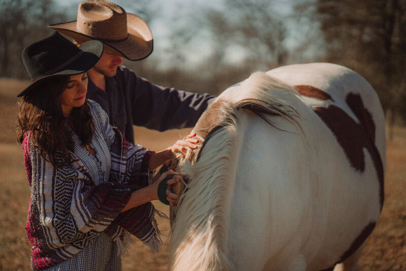 Cowboy and cowgirl brush a rescue horse in the sunset during their elopement.