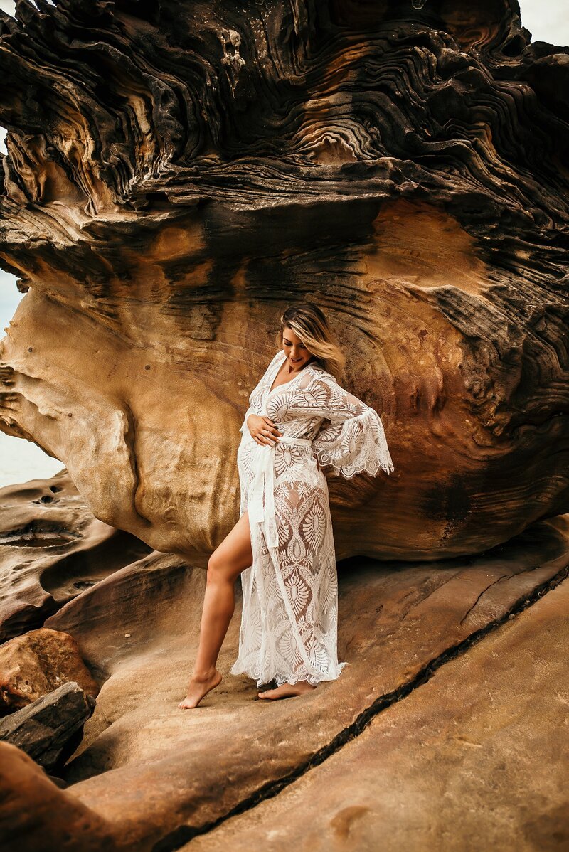 Pregnant woman posing in lace dress near rocks