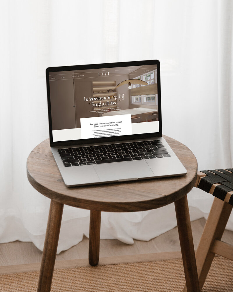 Laptop op houten tafel met open website van Studio Lave, getoond is de pagina over interieurontwerp met warme natuurlijke kleuren