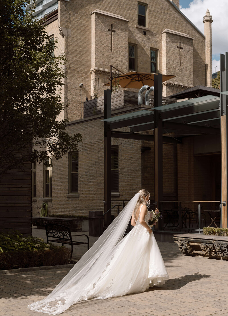 A bride walking in the sun in the courtyard of St. Michael's Basilica in Toronto, Ontario. 