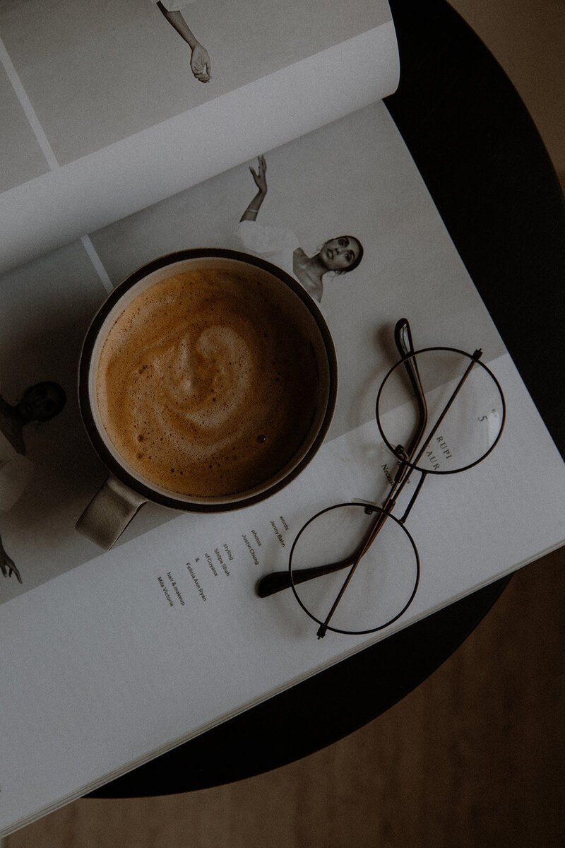 a warm cup of coffee with glasses and a magazine