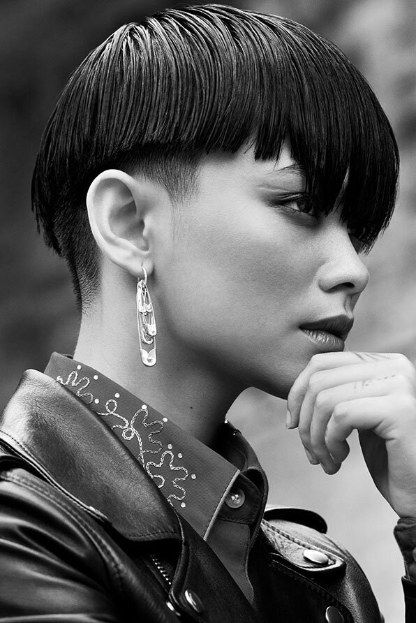 Wet-look cropped hairstyle with undercut detailing, accessorized with a safety pin earring and embroidered leather jacket.