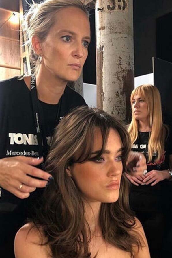 Katy Reeve Hairdresser styling brunette hair backstage at a professional event, with "TONI&GUY" branding visible on clothing.