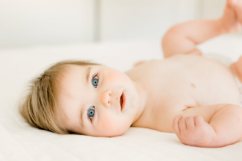 Baby boy with blue eyes laying on bed and looking directly at camera.