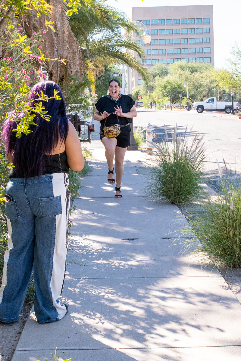 Smiling woman walking down a sunny Tucson sidewalk holding a small patterned purse, photographed by Vyrl Photo, showcasing Tucson brand photography.