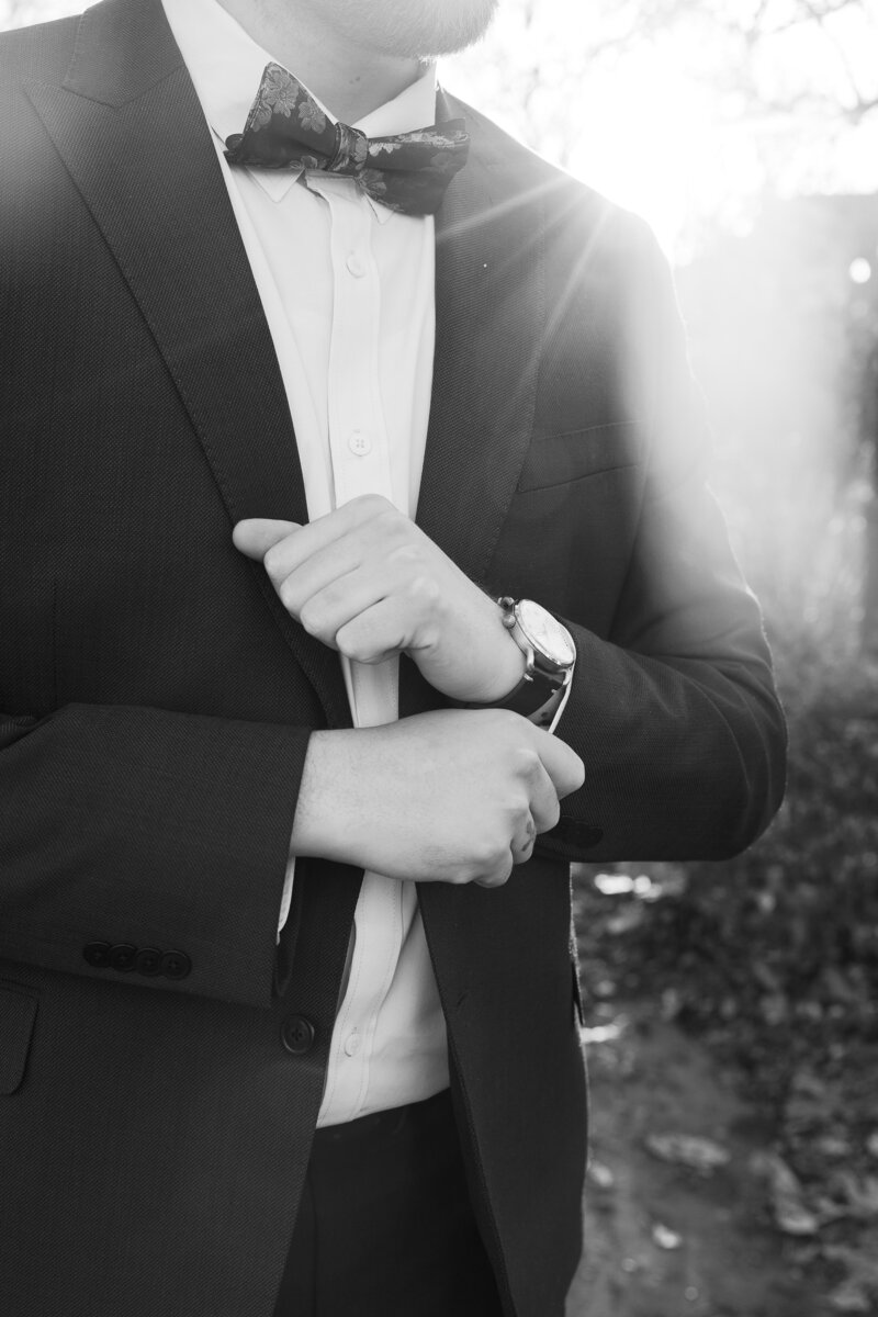 A groom pulls the cuff of the sleeve of his suit, framing his watch.