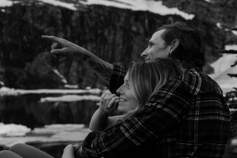 a black and white image of us snuggling in a mountain landscape. Kyle Points as Sam smiles following the direction of his hand