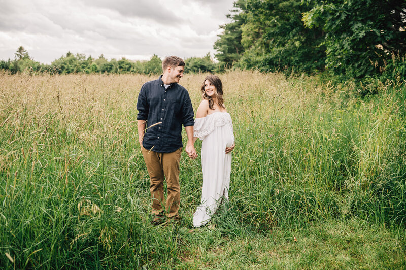 Couple in field, looking down at pregnant mom's belly