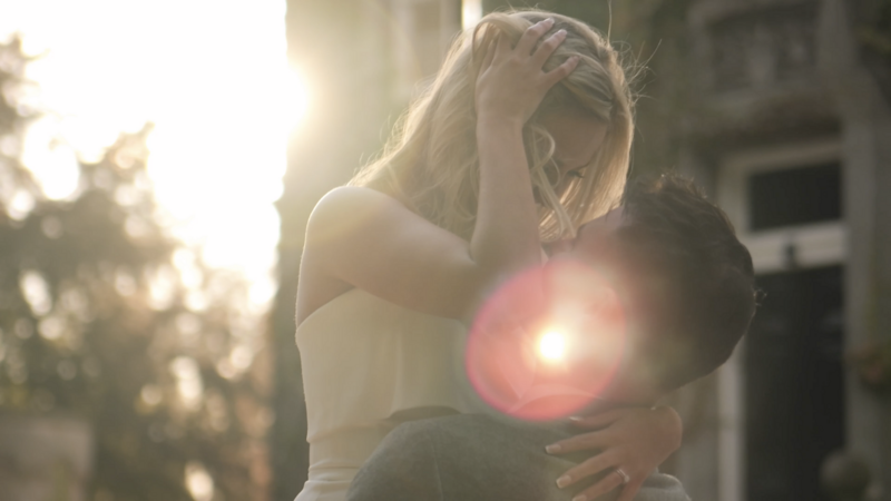 Bride in grooms arms during golden hour with sun flare on the image. 