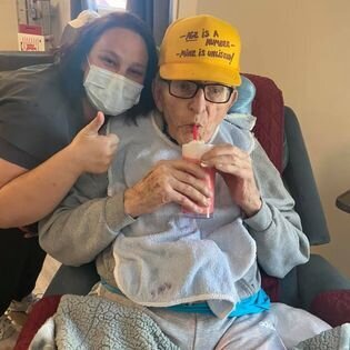 Resident of Creekstone assistedd living drinking a smoothie  and smiling with a staff member