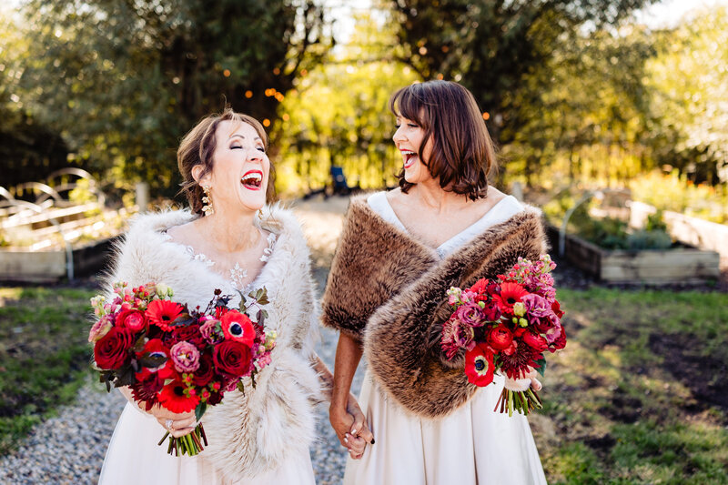 Two brides laughing and walking through the gardens at Cornman Farms in Dexter Michigan
