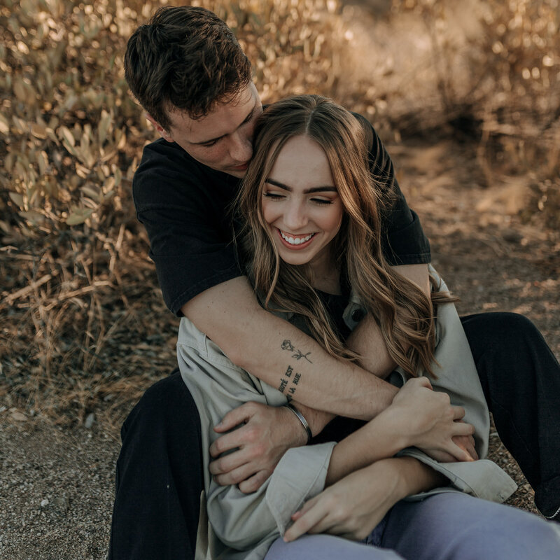 couple with tattoos sitting down for engagement session in the desert