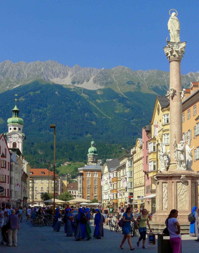 Colorful historic buildings lining Maria-Theresien-Strasse in Innsbruck, with the St. Anne’s Column in the foreground and rugged alpine peaks in the background ©Stephanie Dosch | theViatrix Bespoke Austria Travel Itinerary