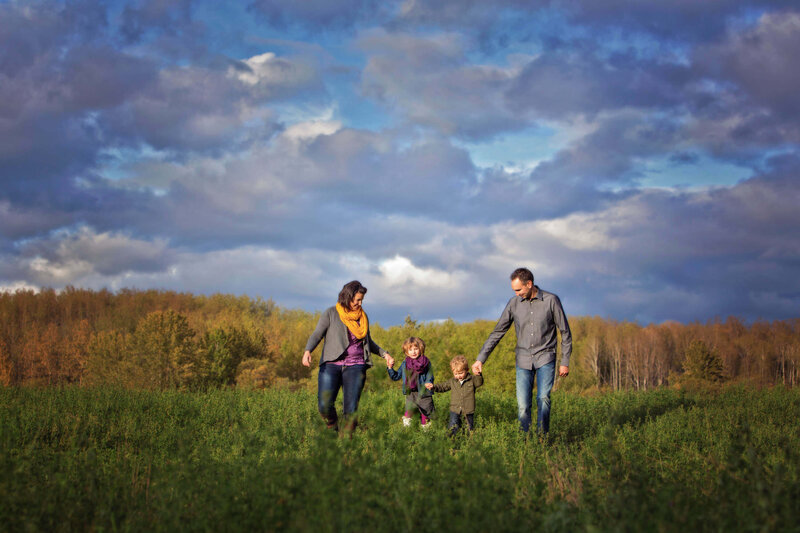 family of 4 holding hands and walking in a hay meadow