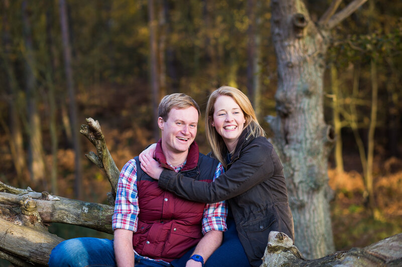 couple smiling in woods on their engagement shoot at Frensham Little Pond in Surrey