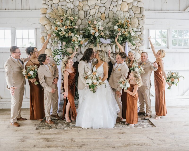 A wedding party cheers as the bride and groom kiss in the Bonnet Island Estate Chapel. A burnt sienna and tan color scheme